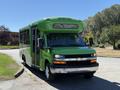 A 2013 Chevrolet Express bus painted bright green with a large front windshield and chrome accents on the bumper and grille