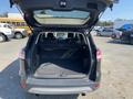 A 2016 Ford Escape with an open rear hatchback revealing a spacious cargo area with a black carpeted floor and no visible items inside