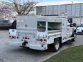 A white 2008 Ford F-450 with a utility bed and storage compartments at the rear equipped with a green pipe