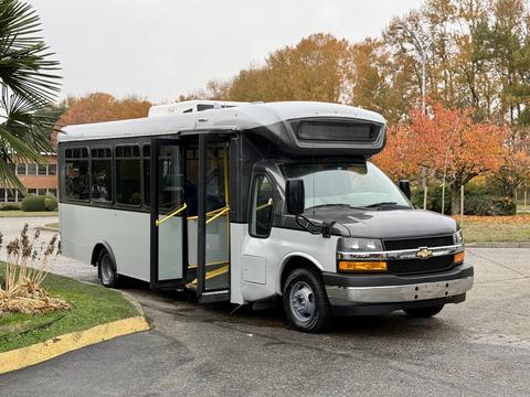 A 2020 Chevrolet Express bus with a black front and white body displaying large windows and an open door for passenger entry