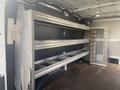A 2017 Ford Transit interior featuring metal shelving units mounted on the walls and a storage compartment door on the right side