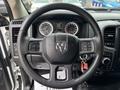Black steering wheel with a RAM logo in the center and control buttons attached on both sides, showcasing the dashboard with gauges and display in the background