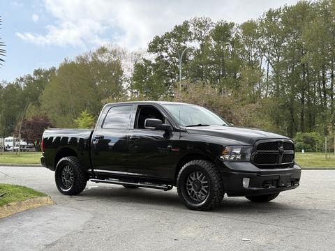 A black 2018 RAM 1500 pickup truck with black wheels parked on a street, featuring a crew cab and rugged tires