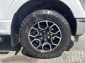 A 2021 Ford F-150 tire featuring a black alloy wheel design with six spokes and bold off-road tread pattern