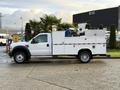 A white 2010 Ford F-550 truck with a service body and equipment storage compartments on either side