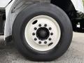 Close-up of a large black tire mounted on a white rim with multiple lug nuts visible around the hub of a 2021 Freightliner M2 106 truck