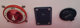 A red switch labeled OFF with a circular design a dark rectangular panel with a small button and a circular socket with a cap marked with the brand name on the right