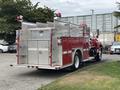 A red 2002 GMC C7500 fire truck with silver equipment compartments and lights on top parked on a concrete surface