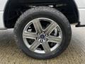 Close-up of a silver wheel and tire from a 2014 Ford F-150 featuring five spokes and a prominent Ford logo in the center