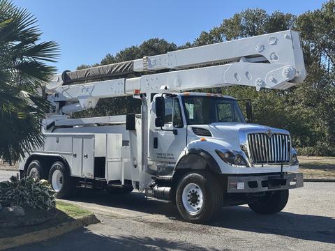 A white 2013 International 7500 bucket truck with an extended boom and equipment storage compartments on the side