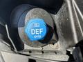 A blue cap labeled DEF only located on a dark surface within a vehicle's engine compartment