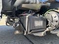 A close-up view of a black battery mounted on a metal bracket with various wires and cables connected to it in a vehicle engine compartment