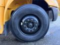 Close-up of a large black tire mounted on a yellow truck wheel with nuts securing it in place