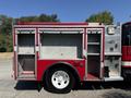 A red 1991 International 4600 fire truck with an open storage compartment showing empty shelves and a white wheel