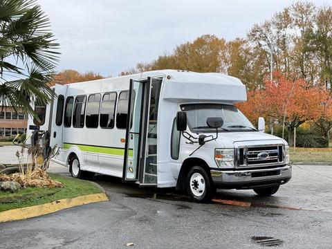 A white 2009 Ford Econoline shuttle bus with a large side door open and green accents on the body
