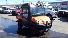 A 2013 Kubota RTV 1100 utility vehicle with an orange and black body featuring a flatbed and a front brush guard