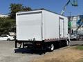 A white 2022 Isuzu NQR box truck is parked with its rear facing the viewer featuring a smooth, unmarked back and utility equipment visible on the side