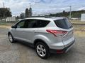 A silver 2015 Ford Escape parked on gravel with a sleek design and tinted windows showing a modern SUV profile