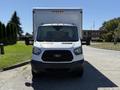 A 2015 Ford Transit van with a white front and a large cargo box attached to the back facing directly towards the viewer