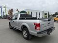 A silver 2015 Ford F-150 pickup truck is shown from the rear at an angle with a tonneau cover on the truck bed and the Ford logo visible on the tailgate