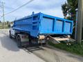 A white 2002 Ford F-550 with a blue dump bed parked on a gravel road