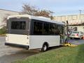 A 2019 Chevrolet Express bus with a white exterior and large windows is parked, featuring a wheelchair lift at the back and a sleek rear design