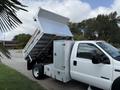 2007 Ford F-450 truck with a raised aluminum dump bed and side storage compartments in a two-tone white and silver color scheme