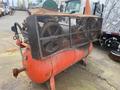 A rusted 2000 Baldor Air compressor with a large air tank and mesh guard covering two fans mounted on top