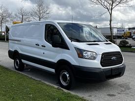 A 2018 Ford Transit van with a white exterior and black accents parked with a side view showing its sliding door and front grille