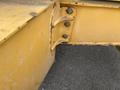 A close-up view of a yellow metal component of a 2012 John Deere 310SJ showing bolts and a slightly worn surface