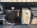 A black fuel tank with a metal cap and a silver tank beside it on a truck's frame