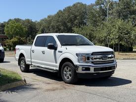 A white 2018 Ford F-150 pickup truck is parked on a driveway with a shiny exterior and chrome details