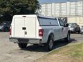 A white 2019 Ford F-150 with a cap on the truck bed is parked at an angle showing its rear view and chrome accents