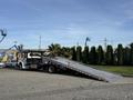 A 2022 Freightliner M2 106 truck with a flatbed ramp extended ready to load vehicles