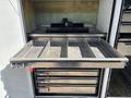 A 2017 Ford F-550 with an open compartment revealing a metal rack system and several trays organized vertically in the foreground