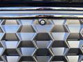 A close-up of a textured gray grille with a round camera lens embedded in the center surrounded by a geometric pattern