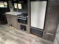 Interior view of a 2021 Jayco Jay Flight camper showing a kitchen area with a stove sink refrigerator and cabinetry on a wood-style floor