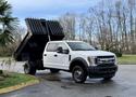 A white 2017 Ford F-450 Super Duty truck with a dump bed raised in the air showcasing its loading capabilities