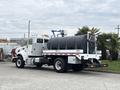 A 2016 Peterbilt 348 truck with a black tank on the back and a ladder mount, featuring a white cab and body with red and white stripes along the lower side