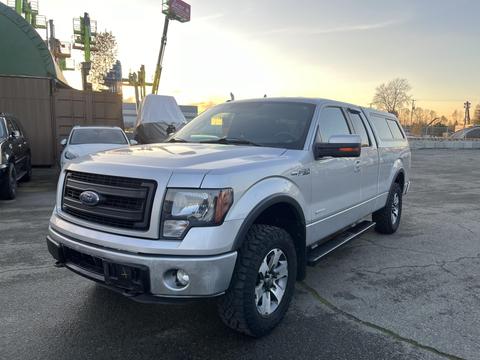 A silver 2014 Ford F-150 pickup truck with a black grille and off-road tires parked on pavement