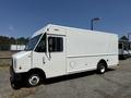 A 2012 Ford Econoline delivery van with a white exterior and side windows parked on a gravel surface