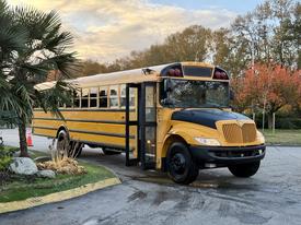 A yellow 2014 International 4300 school bus parked with its door open showcasing its black grille and headlights