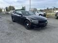 A black 2015 Dodge Charger parked on gravel with a sleek design and black wheels