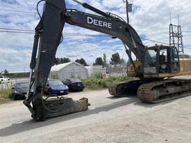 A 2018 John Deere 350 excavator with a long arm and bucket attachment, parked on a road with vehicles in the background