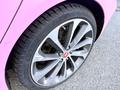 Close-up of a silver alloy wheel with a jaguar emblem and a pink fender of a 2020 Jaguar XE with a textured tire tread visible