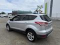 A silver 2014 Ford Escape parked at an industrial site showing its side profile and rear features