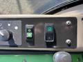 Close-up of control buttons on a 2021 John Deere 1575 featuring two green switches labeled with arrows for up and down movement and a round button illuminated in green