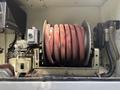 A red coiled hose is stored on a reel attached to a mechanical unit with various gauges and a compressor labeled compressor