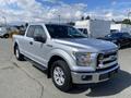 A silver 2015 Ford F-150 with a crew cab and chrome grille parked at an angle showcasing its front and driver side
