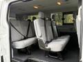 The interior of a 2018 Ford Transit features multiple rows of gray seats with seatbelts visible, arranged for passenger seating in a spacious configuration